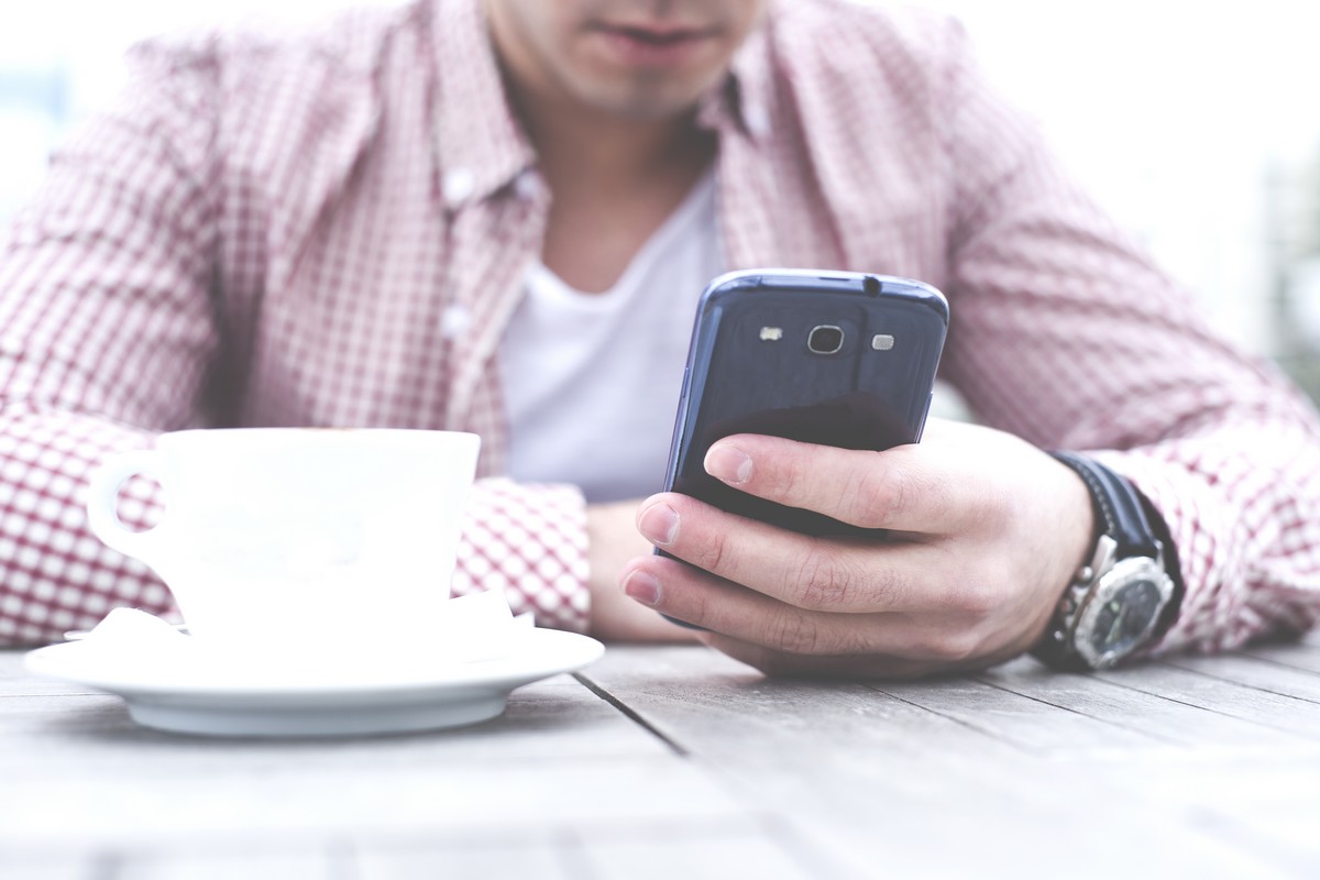 Homme utilise son téléphone et boit un café